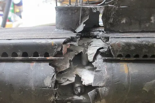 Close-up of a damaged section on a USS Wahoo scale model, showing torn hull plating and exposed internal structure from an explosion effect.