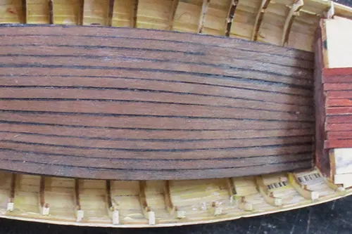 Close-up of a Kyrenia ship model under construction, showing deck planking laid over internal ribs and hull framework.