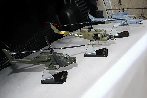 Three Super Wings prototype helicopter models on stands featuring an Apache, Marine UH 1 Huey, and Marine Corps Cobra