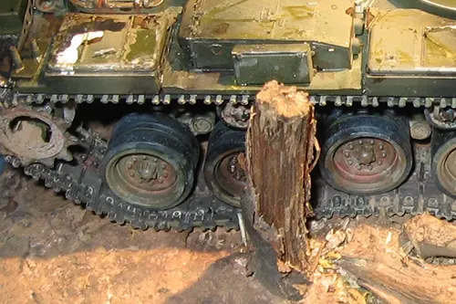 Close-up of M60 tank model treads beside a shattered tree stump with debris from a battlefield scene